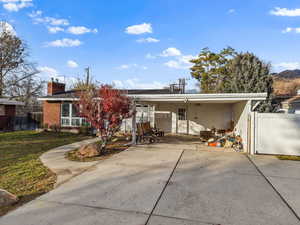 Rear view of property with a chimney, concrete driveway, a carport, and a patio area