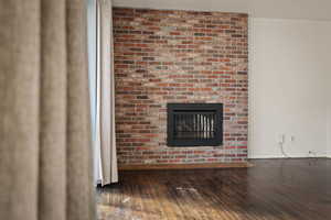 Unfurnished living room with a brick fireplace and dark wood finished floors