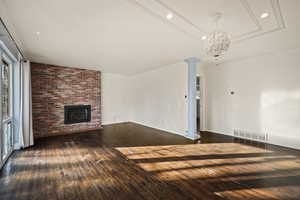 Unfurnished living room featuring recessed lighting, a brick fireplace, dark wood-style floors, and decorative columns