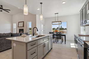 Kitchen with hanging light fixtures, a glass covered fireplace, light wood-style flooring, stainless steel appliances, and light stone counters