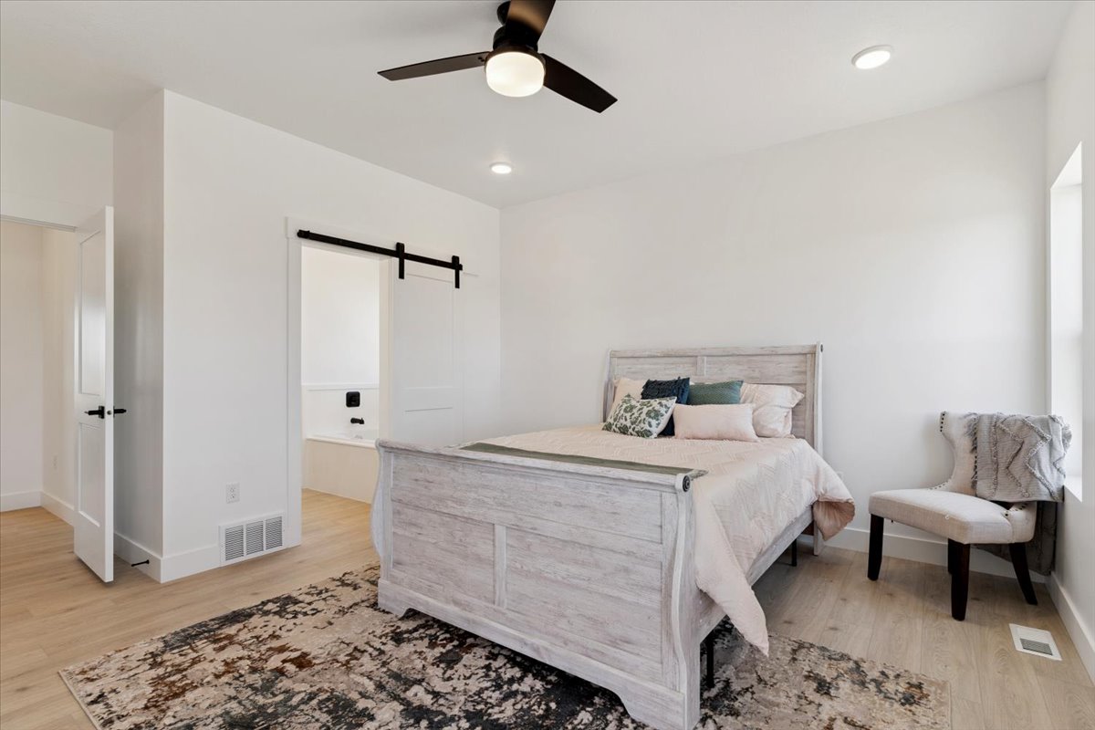 Bedroom with a barn door, light wood-style flooring, and a ceiling fan