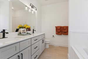 Bathroom with double vanity, light wood finished floors, and a bath