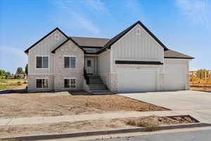 View of front of home with stone siding, board and batten siding, concrete driveway, an attached garage, and roof with shingles