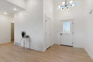 Foyer entrance featuring a chandelier, light wood-style floors, and a towering ceiling