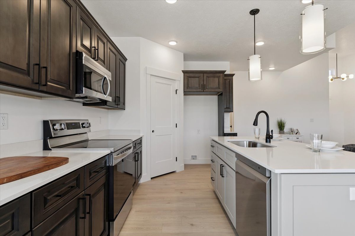 Kitchen featuring appliances with stainless steel finishes, hanging light fixtures, light stone counters, light wood finished floors, and dark brown cabinetry