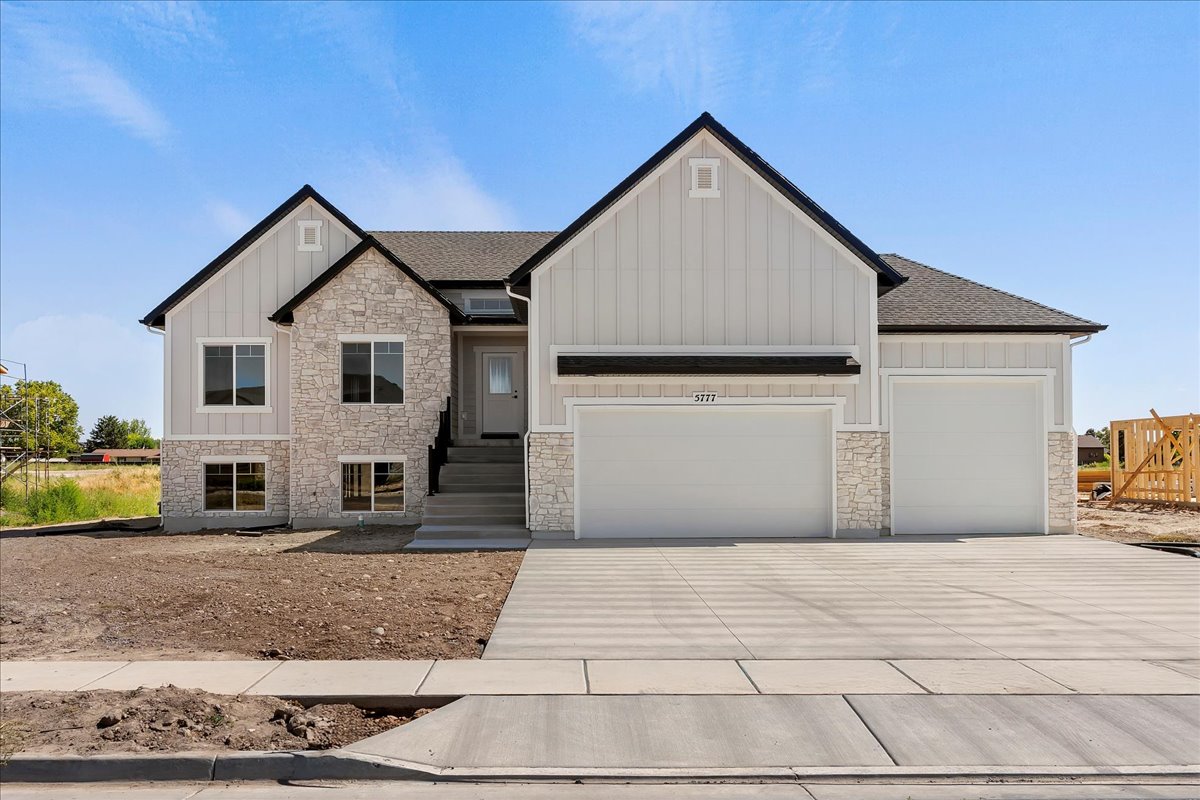 View of front of house with stone siding, board and batten siding, driveway, an attached garage, and a shingled roof