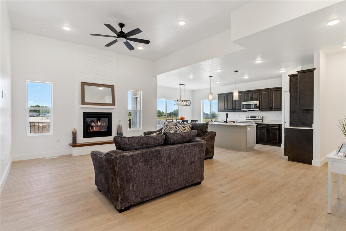 Living area with light wood-style floors, a glass covered fireplace, ceiling fan, and recessed lighting