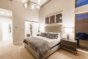 Carpeted bedroom featuring a barn door, a walk in closet, a chandelier, and a high ceiling