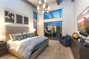 Carpeted bedroom featuring a high ceiling, a chandelier, beam ceiling, and access to exterior