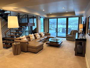 Living area with light carpet, stairway, a raised ceiling, and recessed lighting