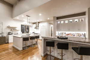 Kitchen featuring a breakfast bar, light stone counters, white cabinets, hanging light fixtures, and light wood-style flooring