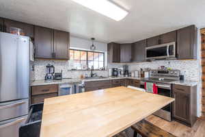 Kitchen featuring stainless steel appliances, dark brown cabinets, a textured ceiling, light stone counters, and light wood finished floors