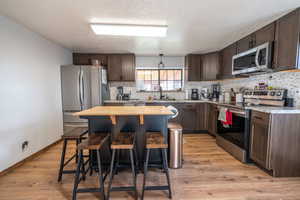 Kitchen featuring stainless steel appliances, dark brown cabinets, a kitchen breakfast bar, light wood-style floors, and a textured ceiling