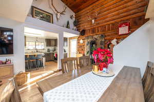 Dining area with light wood finished floors, log walls, a wood stove, and high vaulted ceiling