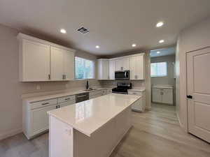 Kitchen with stainless steel appliances, white cabinets, a kitchen island, light wood finished floors, and plenty of natural light