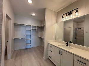 Bathroom featuring vanity, a walk in closet, a shower stall, light wood finished floors, and recessed lighting