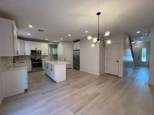 Kitchen featuring white cabinets, decorative light fixtures, a center island, appliances with stainless steel finishes, and light wood-style flooring