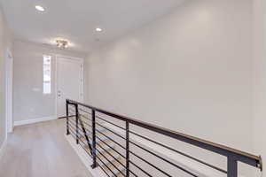 Corridor with an upstairs landing, recessed lighting, and light wood-style flooring