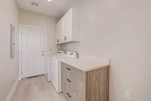 Washroom featuring cabinet space, light wood-style flooring, separate washer and dryer, and electric panel