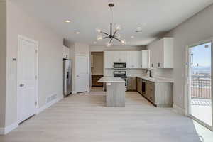 Kitchen featuring a chandelier, light countertops, pendant lighting, appliances with stainless steel finishes, and light wood finished floors