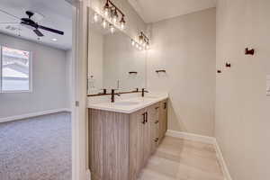 Bathroom with double vanity, light colored carpet, and ceiling fan