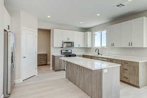 Kitchen featuring appliances with stainless steel finishes, light wood-style flooring, white cabinets, light stone counters, and recessed lighting