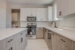 Kitchen featuring appliances with stainless steel finishes, white cabinets, light stone counters, light wood-style flooring, and light brown cabinetry