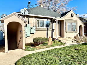 View of front facade with stucco siding, roof with shingles, and a front yard
