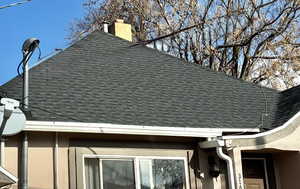 Exterior view of a shingled roof, a downspout, a chimney, gutters, and stucco siding