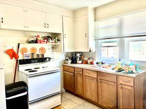 Kitchen with white appliances, light countertops, light tile patterned flooring, brown cabinetry, and open shelves