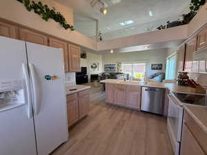Kitchen with open floor plan, white appliances, light countertops, light brown cabinetry.