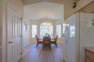 Dining area featuring light wood-style LVP flooring, vaulted ceiling, and a chandelier