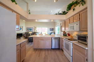 Kitchen featuring open floor plan, white appliances, light brown cabinets, and light countertops