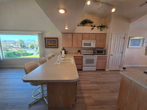 Kitchen with a breakfast bar, white appliances, vaulted ceiling, light countertops, and Plant shelves