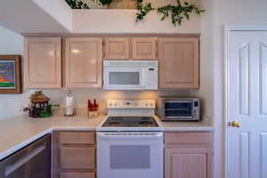 Kitchen featuring light brown cabinets, white appliances, and light countertops
