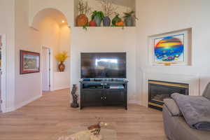 Living room with light wood finished floors, a glass covered fireplace, arched walkways, and a towering ceiling
