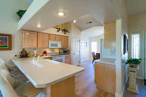 Kitchen with light brown cabinetry, light countertops, a kitchen breakfast bar, and white appliances