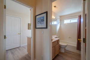 2nd Bathroom featuring vanity, light wood-type flooring, and shower / bathtub combination with curtain and laundry room & garage entrance just beyond