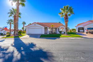 Mediterranean / spanish-style house featuring driveway, a front lawn, an attached garage, a tiled roof, and stucco siding