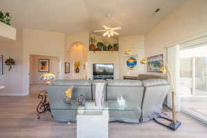 Living room featuring light wood-style LVP flooring, a ceiling fan, arched walkways, and high vaulted ceiling