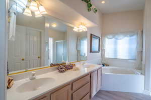 Full primary bath with double vanity, a shower stall, a bath, a chandelier, and light wood-type  LVP flooring