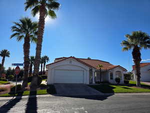 Mediterranean / spanish home with an attached garage, driveway, a tiled roof, stucco siding, and a front lawn