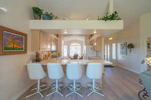 Kitchen featuring light countertops, a kitchen bar, a peninsula, light brown cabinets, and lofted ceiling