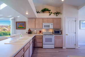 Kitchen featuring white appliances, light brown cabinetry, light countertops, light wood-type flooring, and recessed lighting