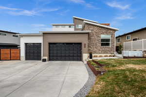 View of front facade featuring driveway, stone siding, and a garage
