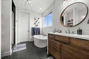 Full primary bath with vanity, a freestanding bath, dark tile patterned floors, and a chandelier