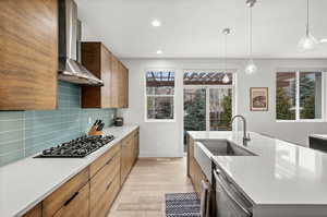 Kitchen with decorative light fixtures, wood finish cabinets, light wood-style flooring, light stone countertops, and dishwasher