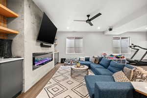 Living room with light wood-style floors, ceiling fan, a glass covered fireplace, and recessed lighting