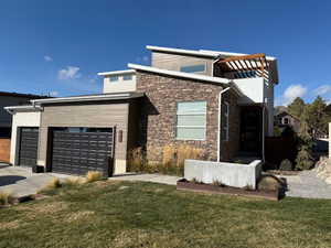 Modern home with driveway, a front yard, and stone siding