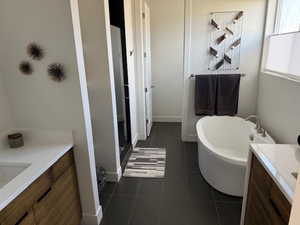 Full bath featuring a freestanding bath, two vanities, a shower stall, and dark tile patterned flooring